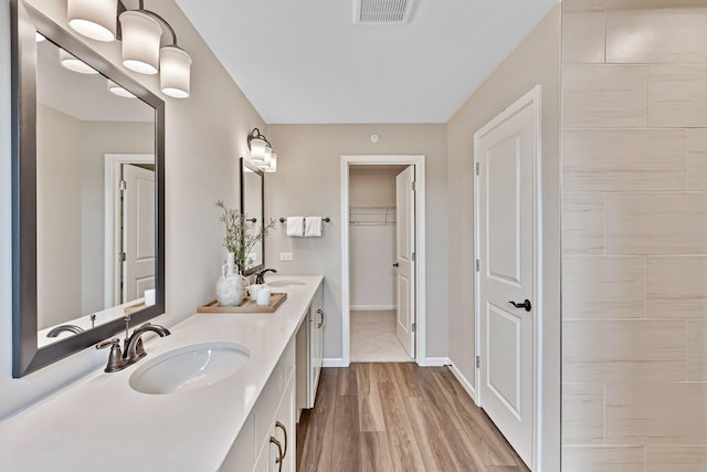 full bath with a sink, double vanity, wood finished floors, and visible vents