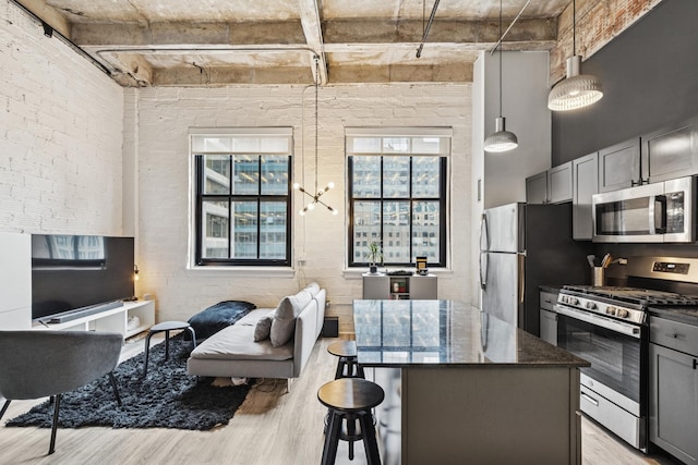 kitchen featuring gray cabinets, appliances with stainless steel finishes, dark stone countertops, light wood-style floors, and a breakfast bar