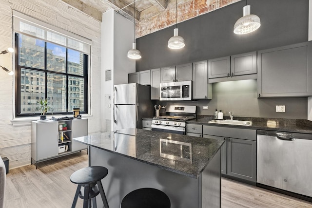 kitchen featuring a towering ceiling, a sink, light wood-style flooring, stainless steel appliances, and a kitchen bar