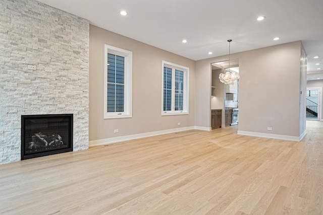 unfurnished living room with light wood-style floors, a stone fireplace, baseboards, an inviting chandelier, and recessed lighting