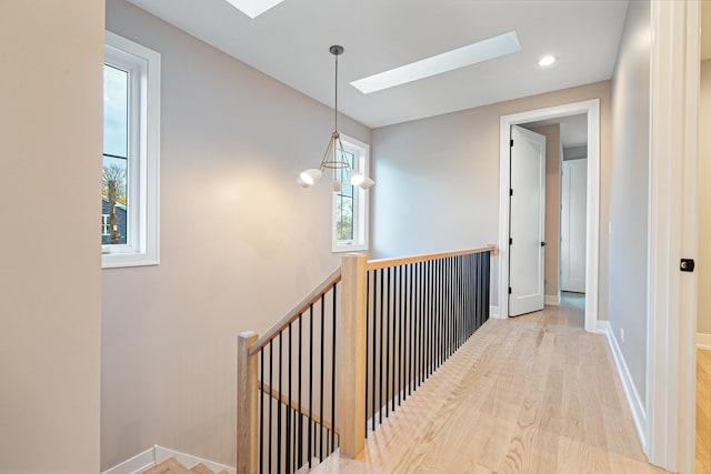 corridor featuring baseboards, an upstairs landing, wood finished floors, and a skylight