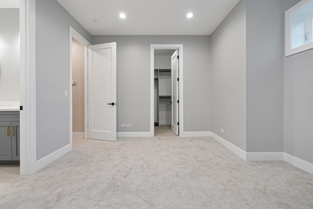 unfurnished bedroom with light colored carpet, a walk in closet, recessed lighting, baseboards, and a closet