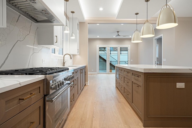 kitchen with wall chimney range hood, light stone countertops, a sink, high end range, and light wood-type flooring