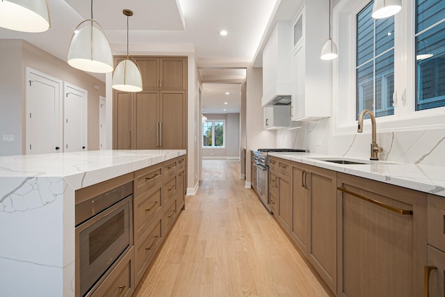 kitchen with brown cabinetry, baseboards, a sink, light wood-style flooring, and appliances with stainless steel finishes