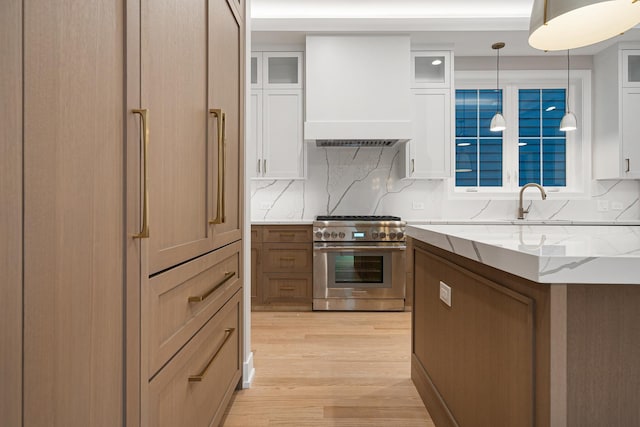 kitchen featuring high end range, white cabinetry, light stone countertops, and light wood-style floors