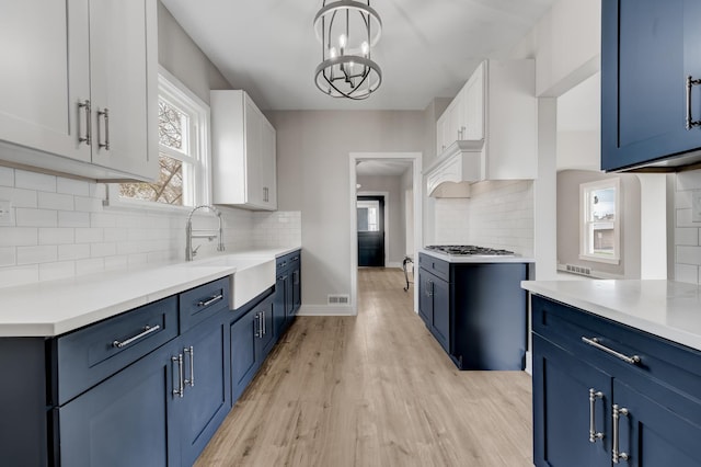 kitchen with backsplash, blue cabinetry, a sink, white cabinets, and light wood-style floors
