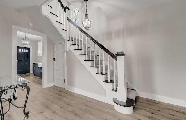 staircase with an inviting chandelier, baseboards, and wood finished floors