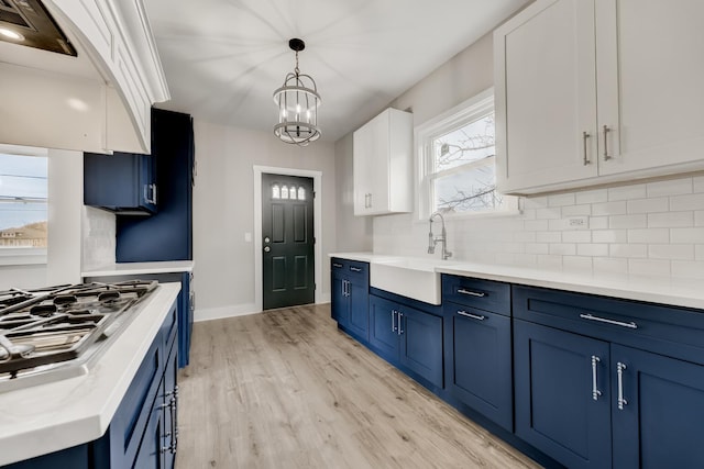 kitchen featuring blue cabinetry, decorative backsplash, a sink, and light wood-style floors