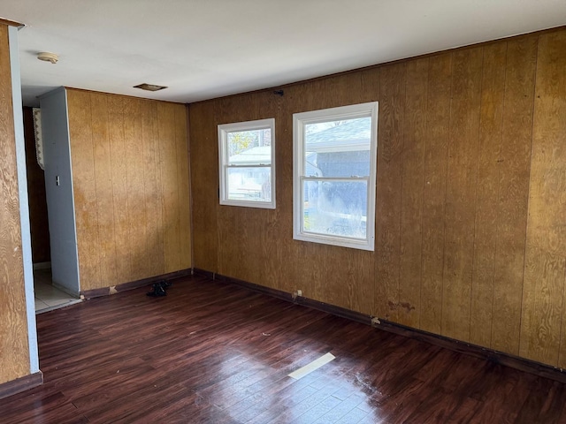 unfurnished room with baseboards, wood finished floors, and wooden walls
