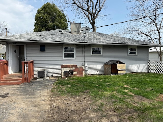 rear view of property featuring roof with shingles, central air condition unit, a chimney, and a yard