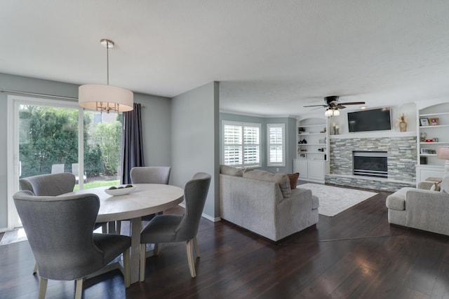 dining room with a ceiling fan, dark wood-style flooring, a stone fireplace, and a wealth of natural light