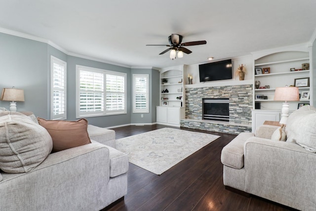 living room with crown molding, dark wood finished floors, a stone fireplace, built in shelves, and a ceiling fan
