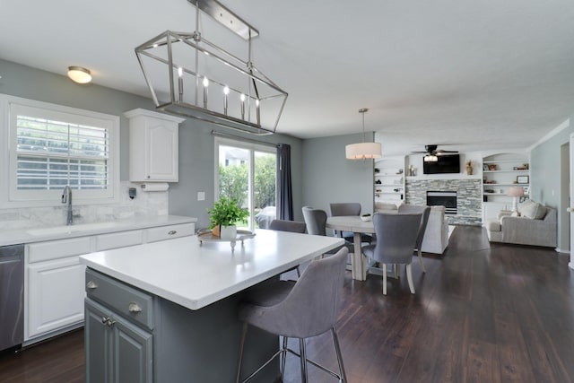 kitchen featuring a fireplace, a sink, light countertops, white cabinets, and dark wood-style floors