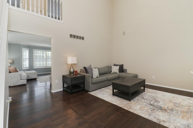 living room featuring baseboards, visible vents, wood finished floors, and a towering ceiling