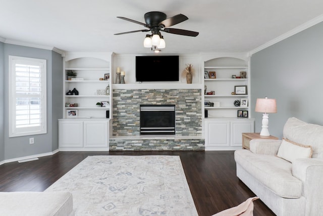 living area featuring a ceiling fan, crown molding, built in features, a fireplace, and dark wood-style floors