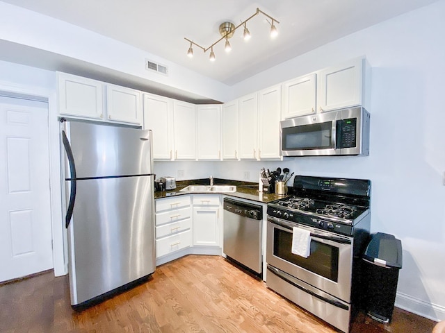 kitchen featuring white cabinets, a sink, stainless steel appliances, light wood-type flooring, and visible vents