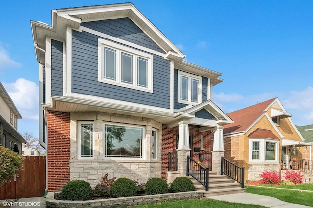 craftsman-style house with fence, stone siding, and a front lawn