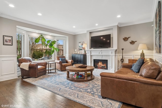 living area with ornamental molding, wainscoting, a decorative wall, wood finished floors, and a high end fireplace