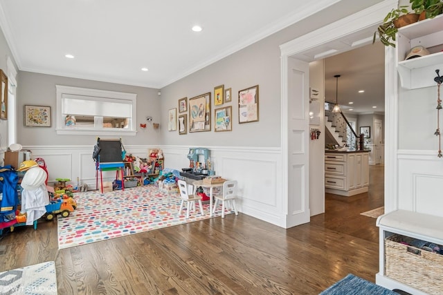 recreation room featuring wood finished floors, ornamental molding, a decorative wall, and a wainscoted wall