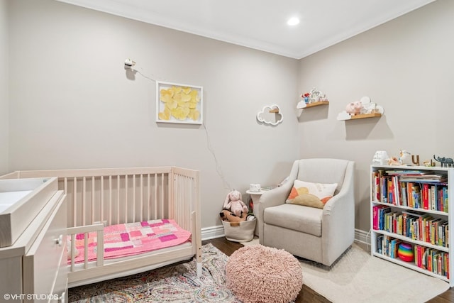bedroom with a nursery area, ornamental molding, baseboards, and wood finished floors