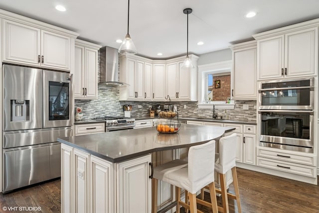 kitchen featuring dark countertops, dark wood-style floors, wall chimney range hood, appliances with stainless steel finishes, and backsplash