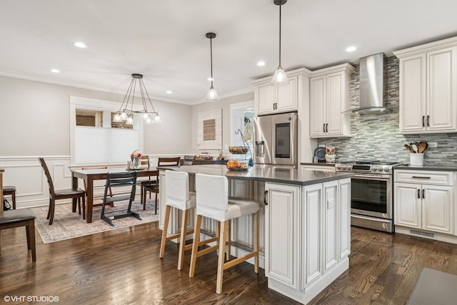 kitchen featuring wall chimney range hood, a kitchen breakfast bar, a kitchen island, dark countertops, and stainless steel appliances