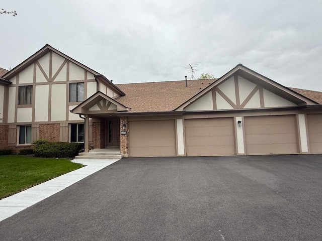 tudor-style house with a shingled roof, an attached garage, brick siding, stucco siding, and driveway