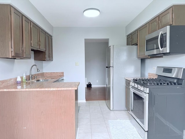 kitchen featuring appliances with stainless steel finishes, light countertops, baseboards, a sink, and light tile patterned flooring