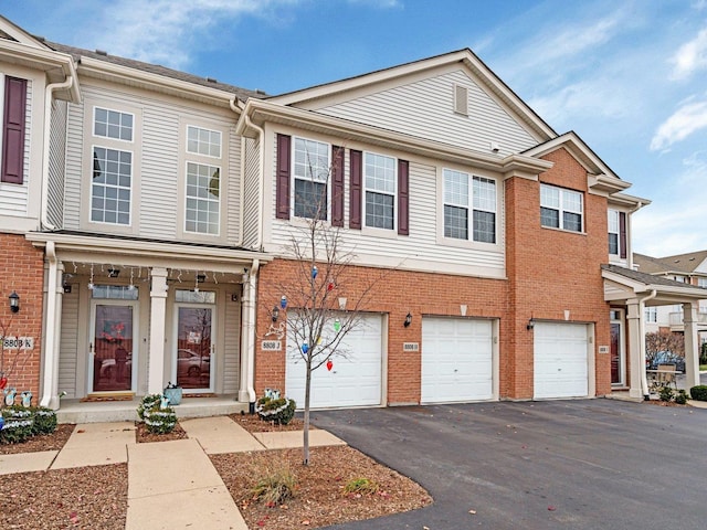 townhome / multi-family property with brick siding, an attached garage, and driveway