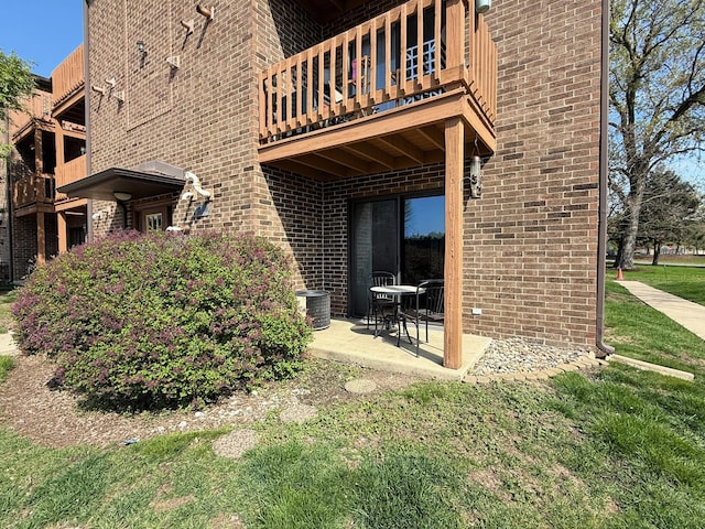 back of house featuring a balcony, brick siding, a patio area, central AC, and a lawn