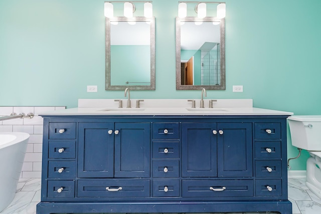 full bath featuring marble look tile flooring, a freestanding bath, double vanity, and toilet