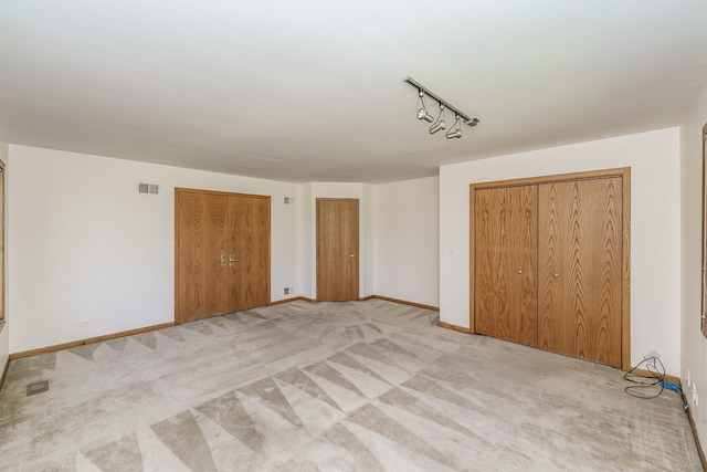 unfurnished bedroom featuring light carpet, two closets, baseboards, and track lighting