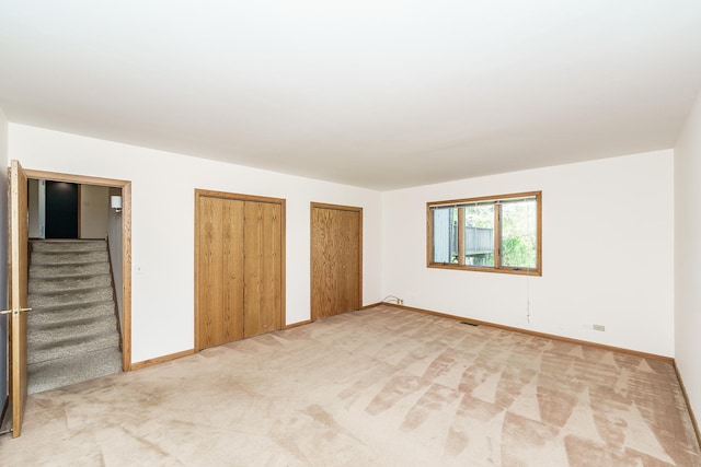 unfurnished bedroom with multiple closets, light colored carpet, and baseboards