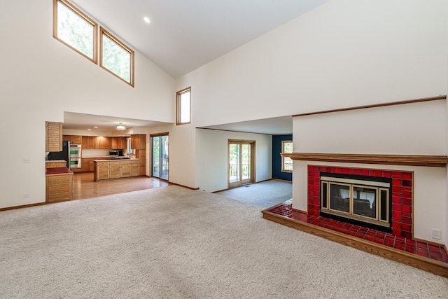 unfurnished living room featuring light colored carpet, a high ceiling, a brick fireplace, baseboards, and recessed lighting