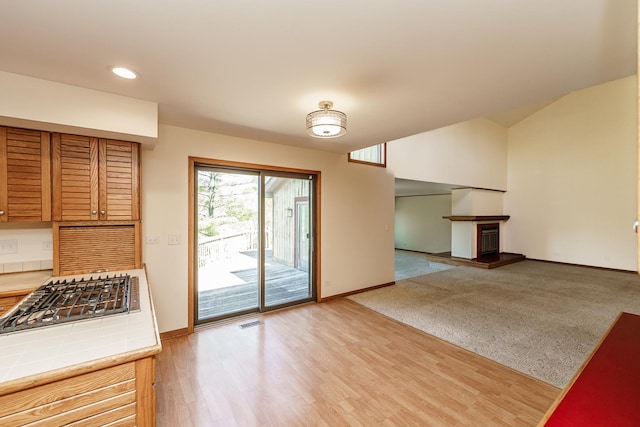 entryway featuring baseboards, a fireplace with raised hearth, recessed lighting, light wood-style flooring, and lofted ceiling