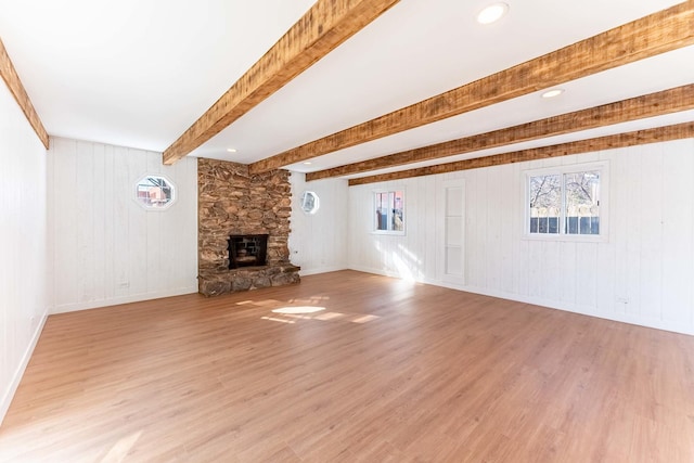 unfurnished living room with light wood-style floors, beamed ceiling, a fireplace, and a wealth of natural light