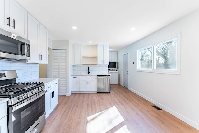 kitchen featuring appliances with stainless steel finishes, open shelves, a sink, light countertops, and washer / dryer