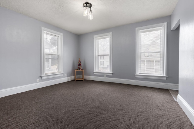 empty room with baseboards, dark carpet, and a textured ceiling