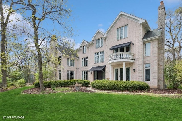 rear view of property featuring a yard, brick siding, a chimney, and a balcony