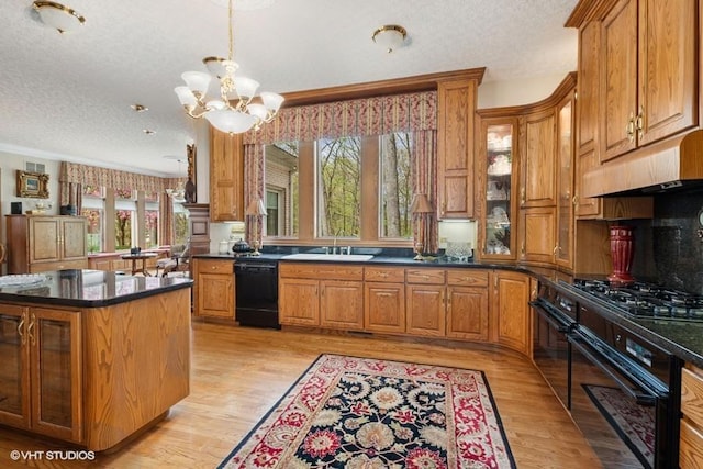kitchen with brown cabinetry, a textured ceiling, under cabinet range hood, and black appliances