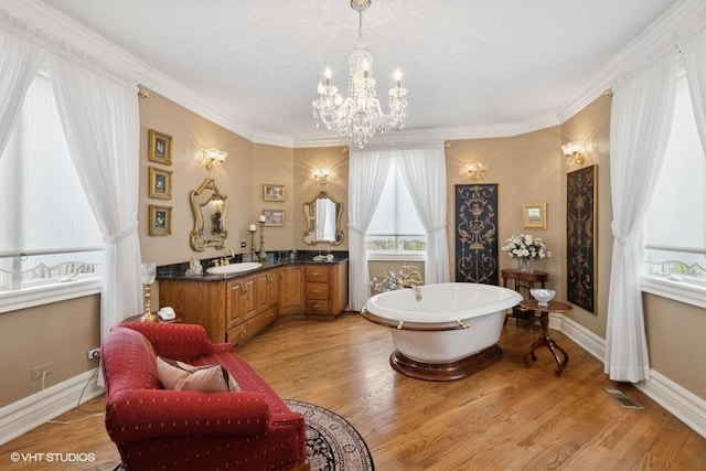 full bathroom with a freestanding tub, a notable chandelier, ornamental molding, and vanity