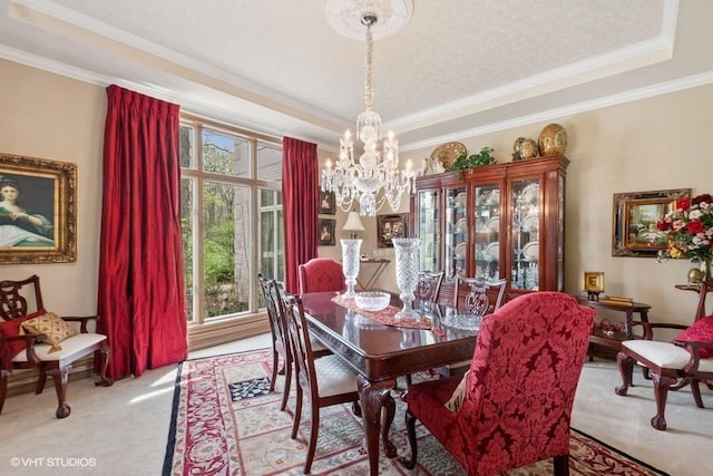 dining space featuring a raised ceiling, ornamental molding, a chandelier, and light colored carpet