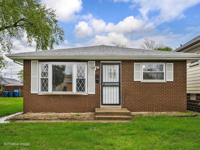 767 May St, Calumet City, IL 60409 - view of front facade with a front yard, brick siding, a wall mounted AC, and a shingled roof