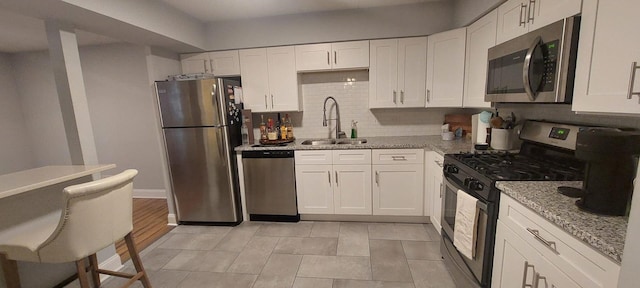 kitchen featuring a sink, light stone counters, white cabinets, and stainless steel appliances