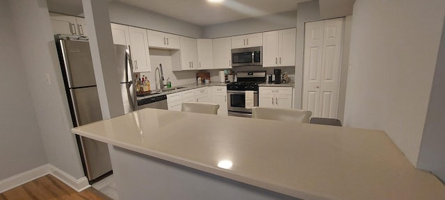 kitchen featuring wood finished floors, baseboards, white cabinetry, a sink, and appliances with stainless steel finishes