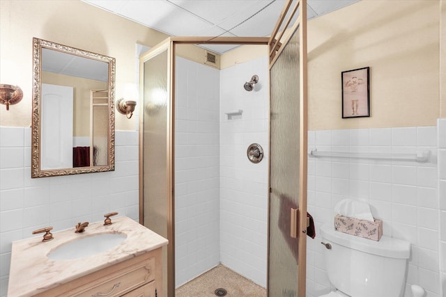 bathroom featuring tile walls, a shower stall, vanity, toilet, and a wainscoted wall
