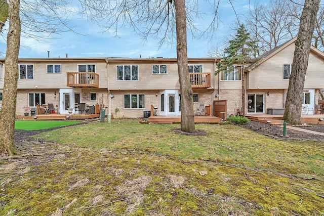 back of house with a lawn, brick siding, a wooden deck, and a balcony