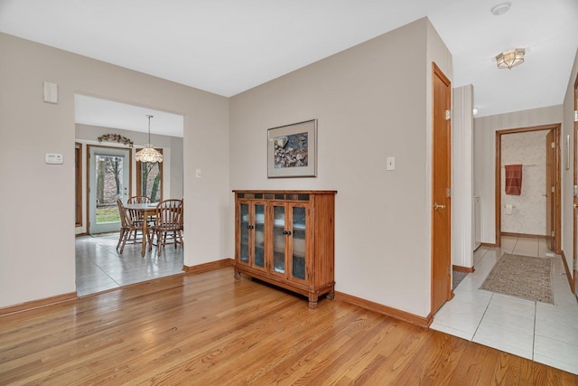 hall with baseboards, a chandelier, and light wood-type flooring