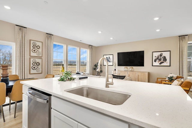 kitchen featuring stainless steel dishwasher, a sink, white cabinets, open floor plan, and recessed lighting
