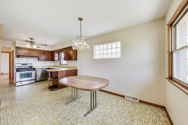 kitchen featuring appliances with stainless steel finishes, light countertops, under cabinet range hood, baseboards, and pendant lighting